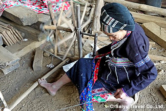 家の軒下で糸車を使い、慣れた手つきで糸を紡ぐルー族の女性